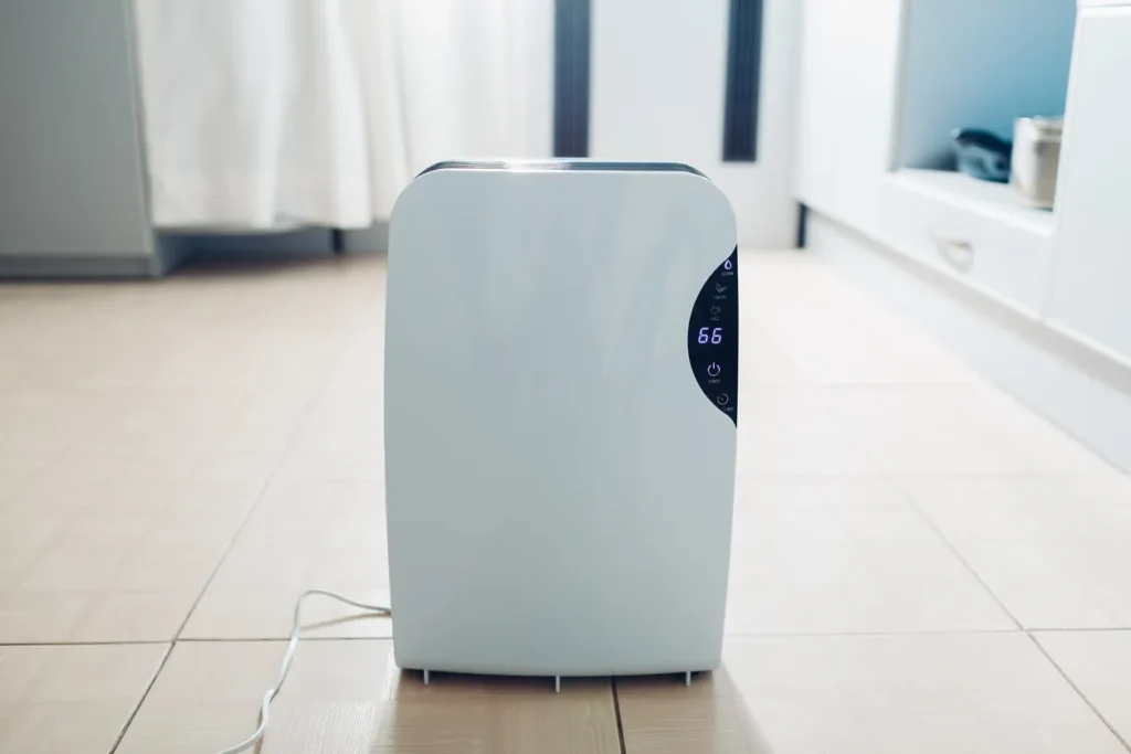 A white dehumidifier stands in a modern living room next to a window