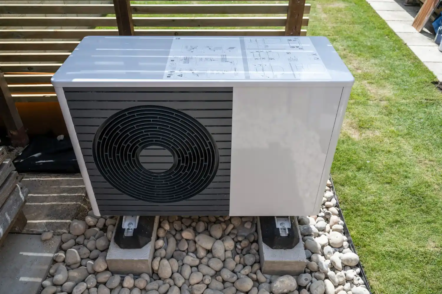 Heating Installation and Replacement in Rainier, WA 2 An outdoor air source heat pump unit, white and gray, sitting on supports surrounded by river stones and grass.
